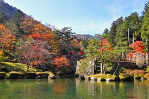 栃木県鹿沼市の古峰神社にある庭園の秋景色。色鮮やかな紅葉と緑の木々が池の水面に映り込み、自然の美しさと静けさが広がる。